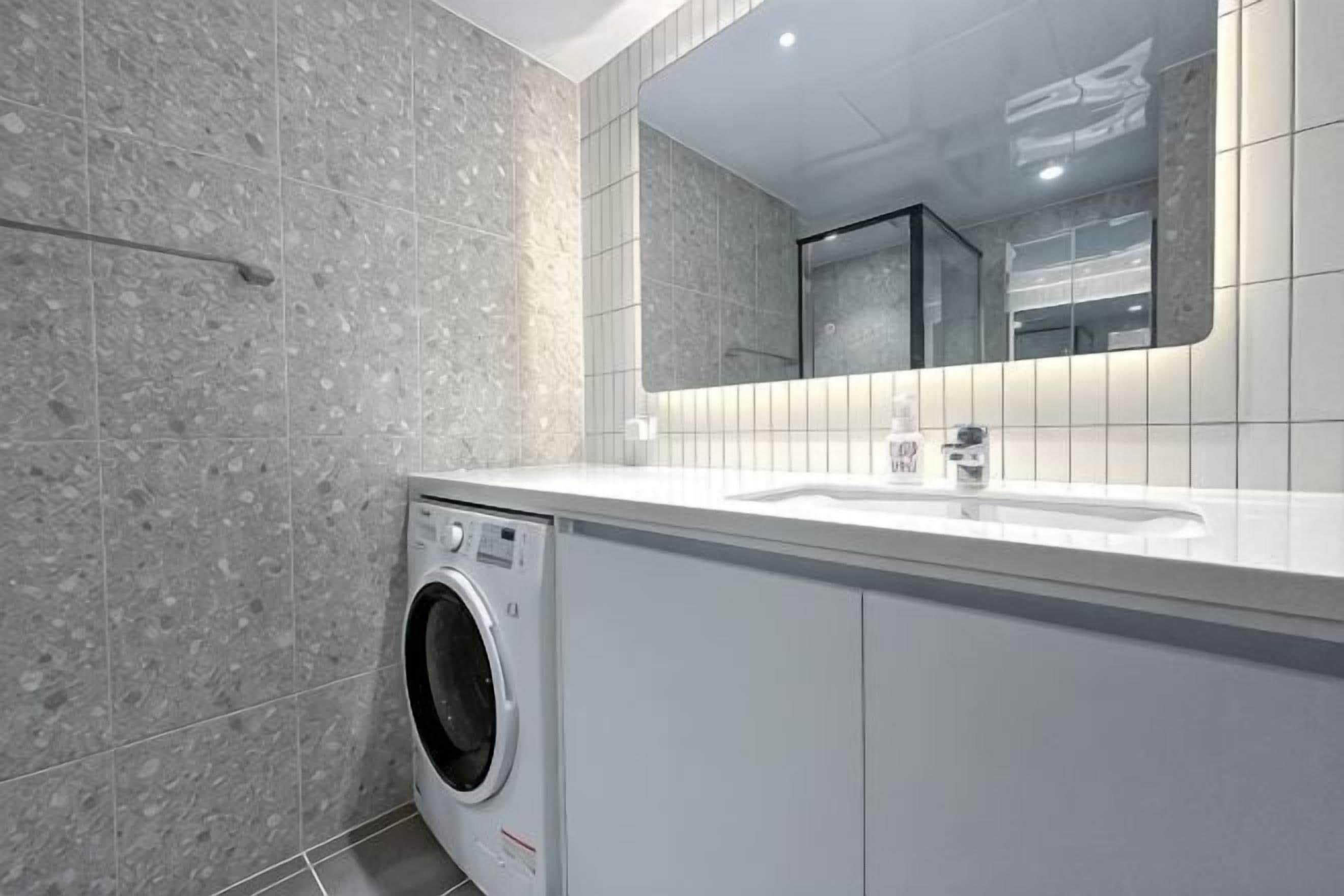 A modern bathroom with a washing machine, a sink, and a mirror.