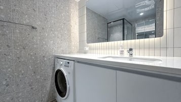 A modern bathroom with a washing machine, a sink, and a mirror.