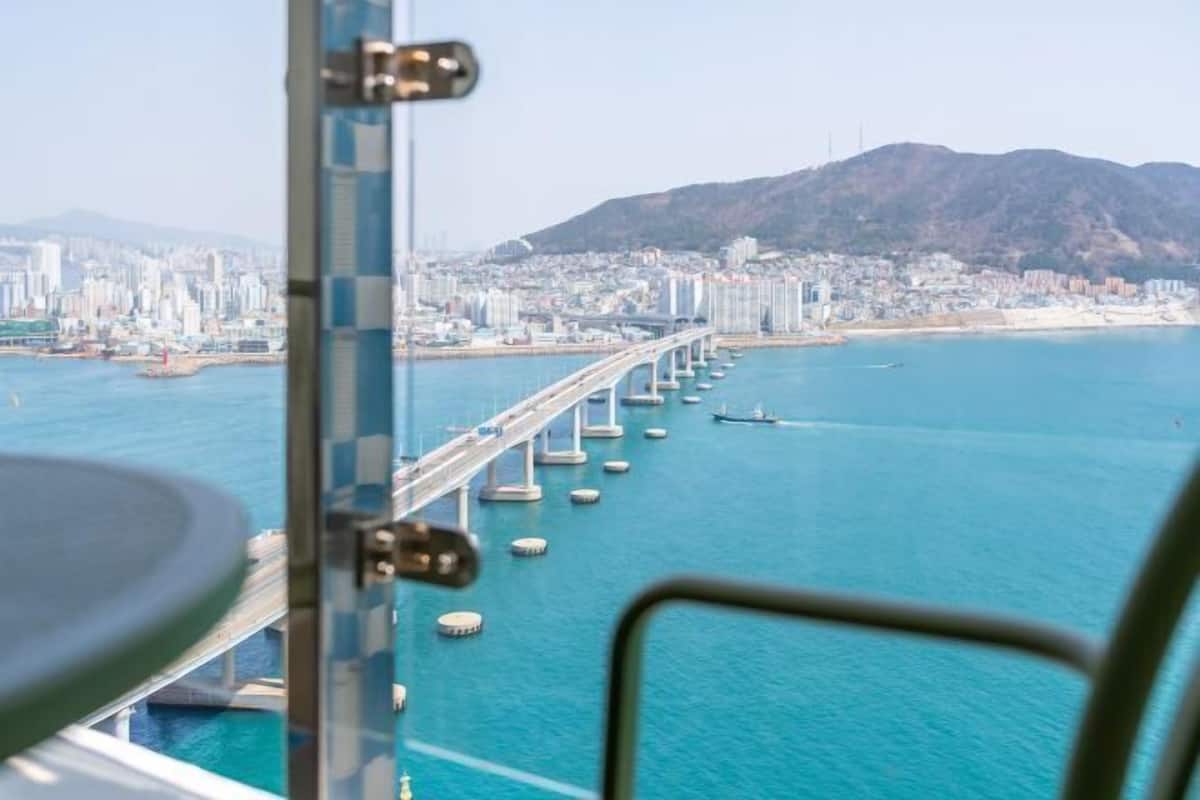A view of a coastal city with a prominent bridge extending into the water, surrounded by high-rise buildings and a hilly landscape.
