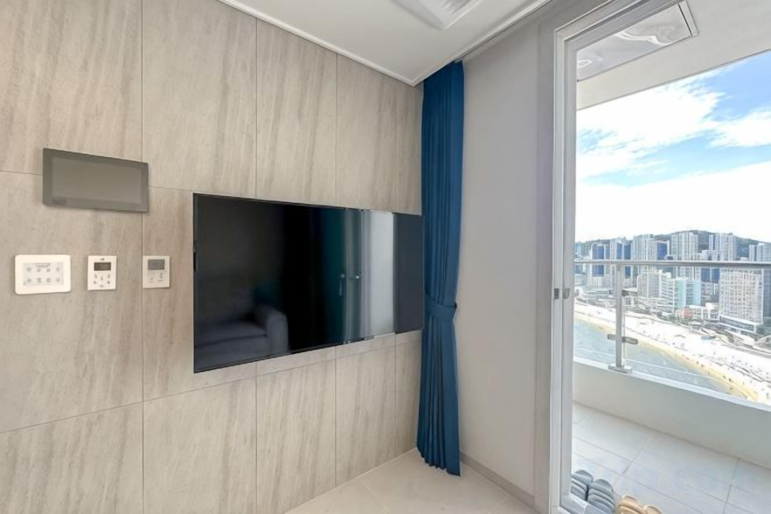 A modern living room with a flat-screen TV, built-in sound system, and a view of a cityscape through a large window.