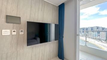 A modern living room with a flat-screen TV, built-in sound system, and a view of a cityscape through a large window.