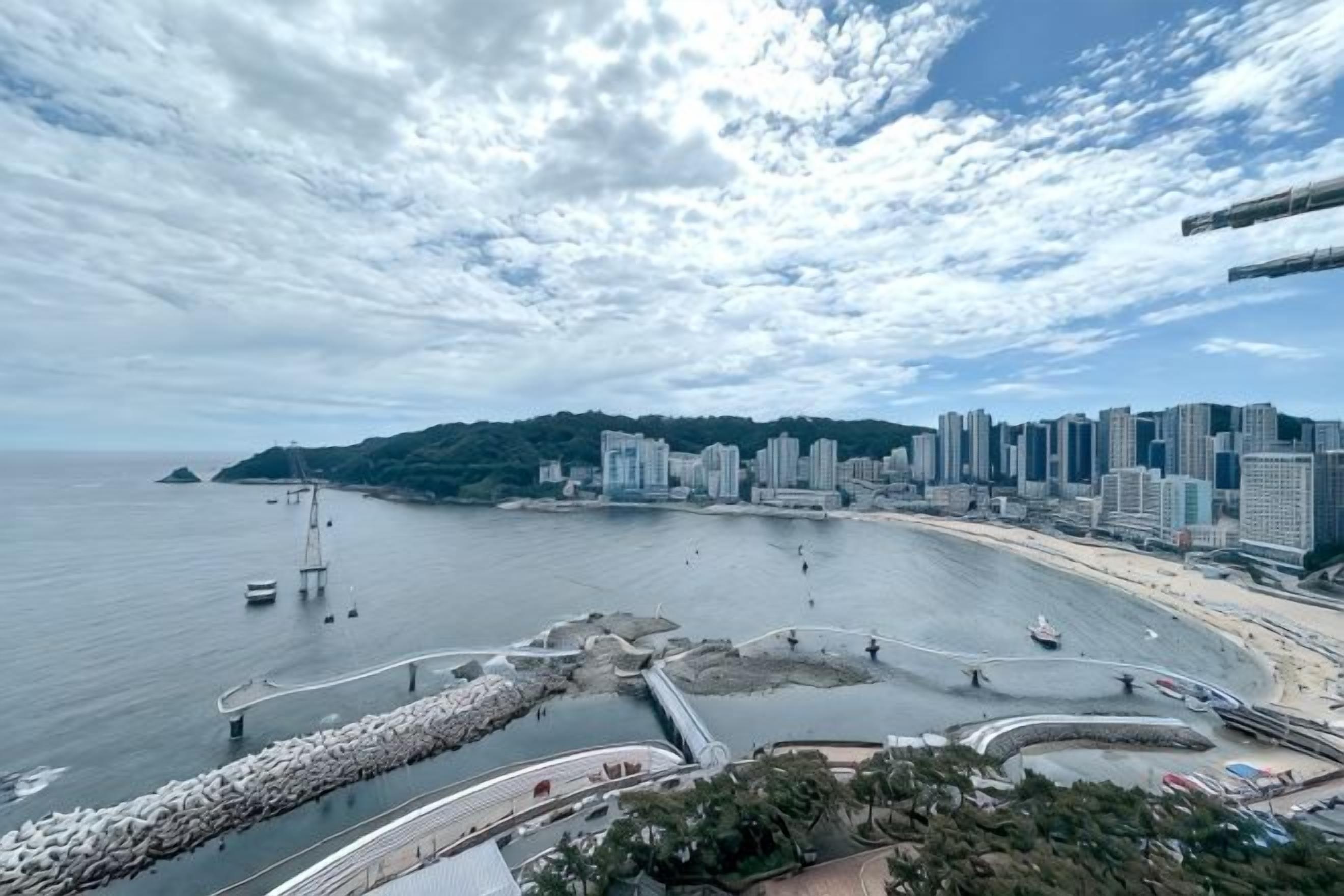 A coastal cityscape with a marina, high-rise buildings, and a curved waterfront promenade.
