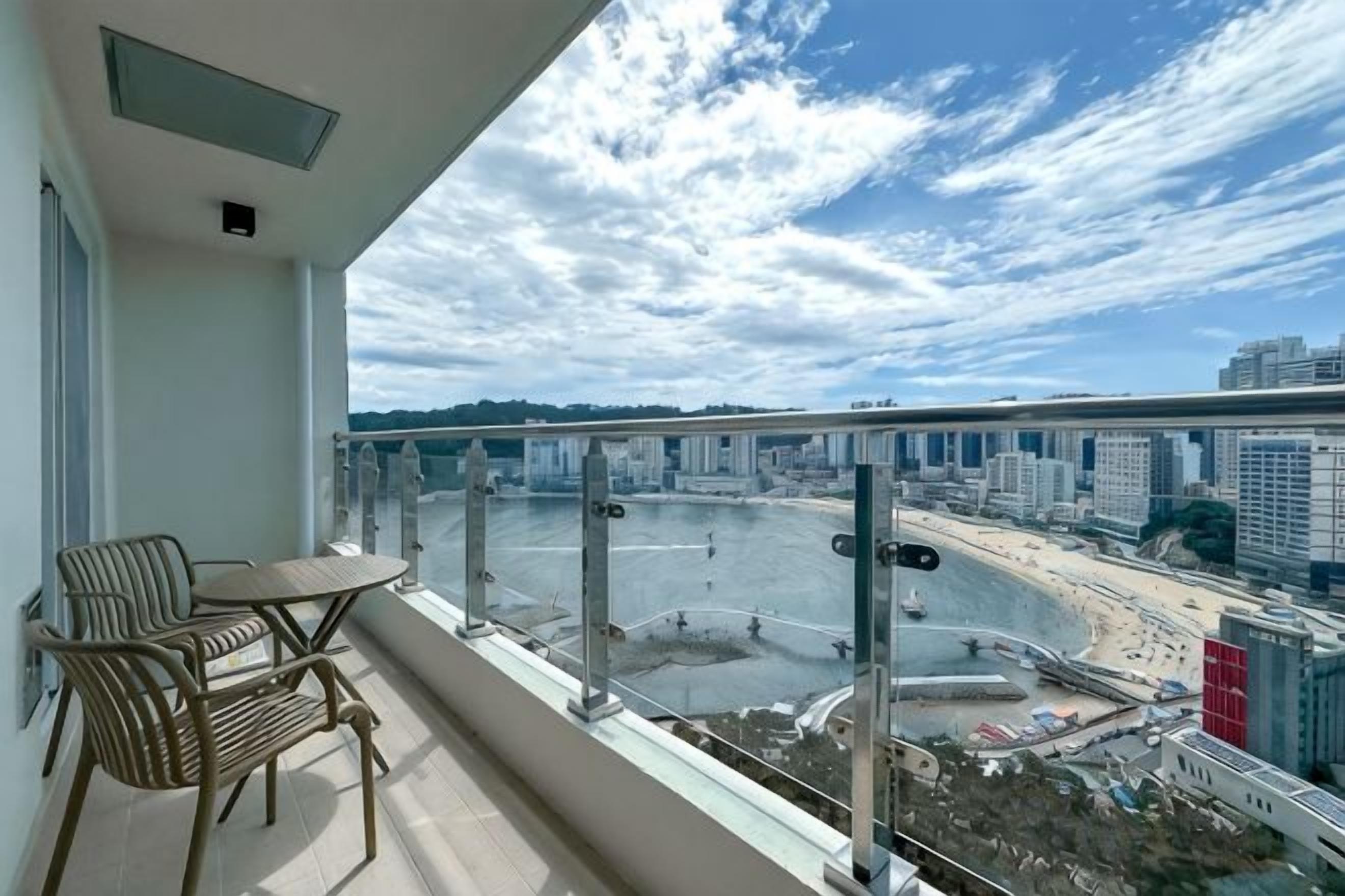 A balcony with a view of a waterfront, a table, and chairs.