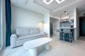 A modern living room with a sofa, a coffee table, and a kitchen area with a bar. - The First Ocean Songdo (Busan)