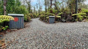 Un chemin de gravier traverse une zone boisée, et on y trouve une barrière en bois et un petit abri.