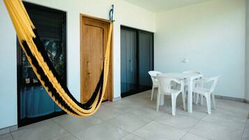 Una habitación con una hamaca, una puerta de madera, una puerta de cristal, una mesa blanca con sillas y un piso de baldosas.