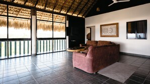 A spacious room with a thatched roof, a sofa, a flat-screen TV, and framed artwork on the walls. - Bungalows Oasis (Brisas de Zicatela)