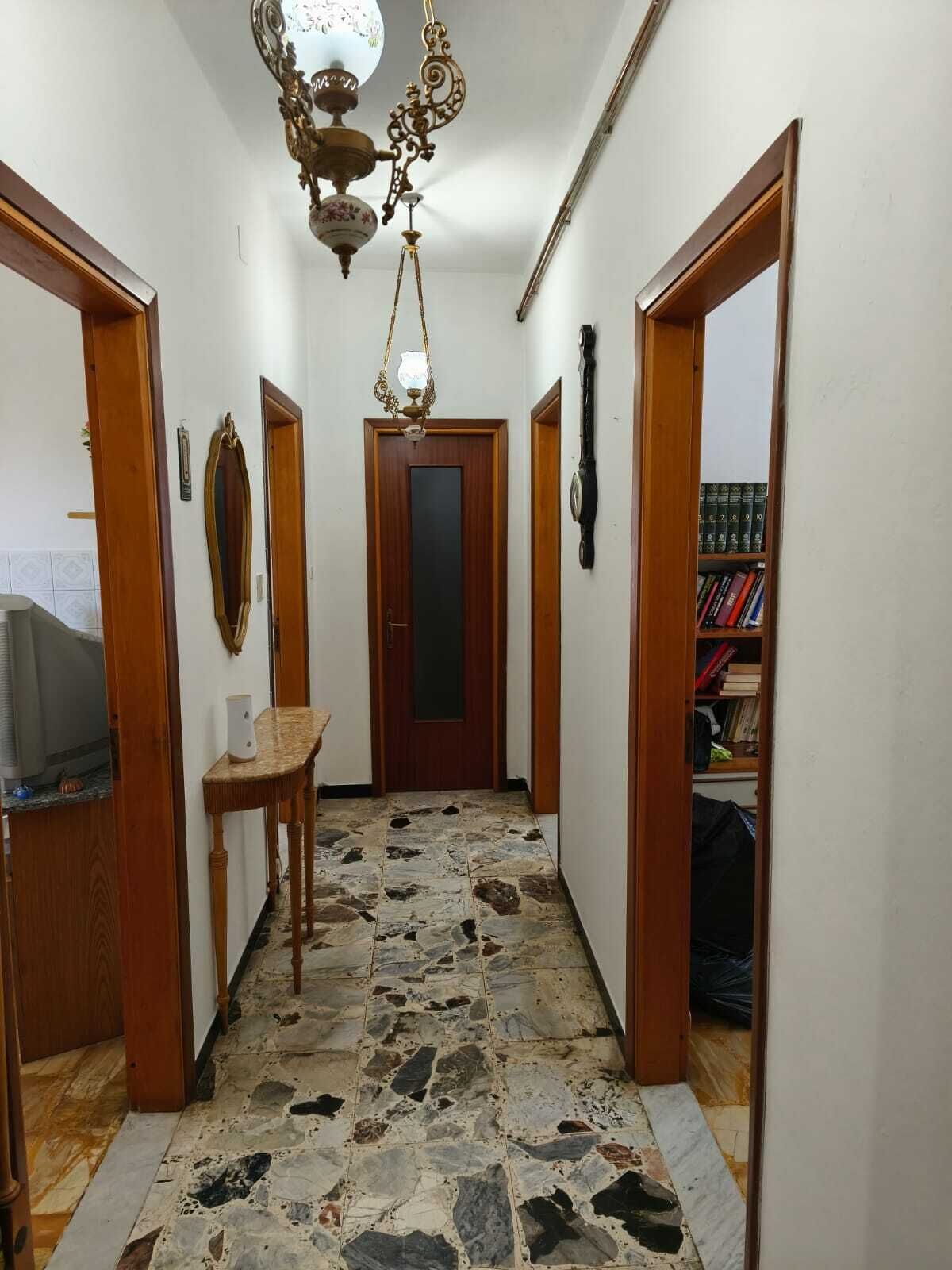 A hallway with a stone floor, wooden doors, a wooden table, and a chandelier.