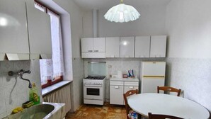 A compact kitchen with white cabinets, a gas stove, a refrigerator, and a dining table with chairs. - Regina Margherita Apartment (Rocchetta Ligure)