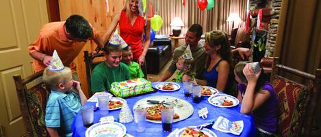 Una familia reunida alrededor de una mesa con un pastel de cumpleaños, platos de comida y bebidas.