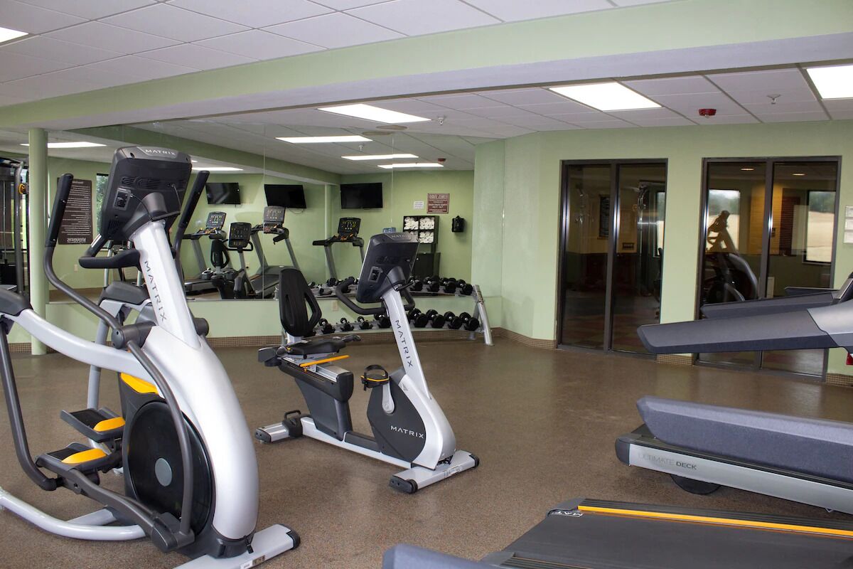 Ein Fitnessstudio mit verschiedenen Cardiogeräten, Kurzhanteln und Laufbändern.