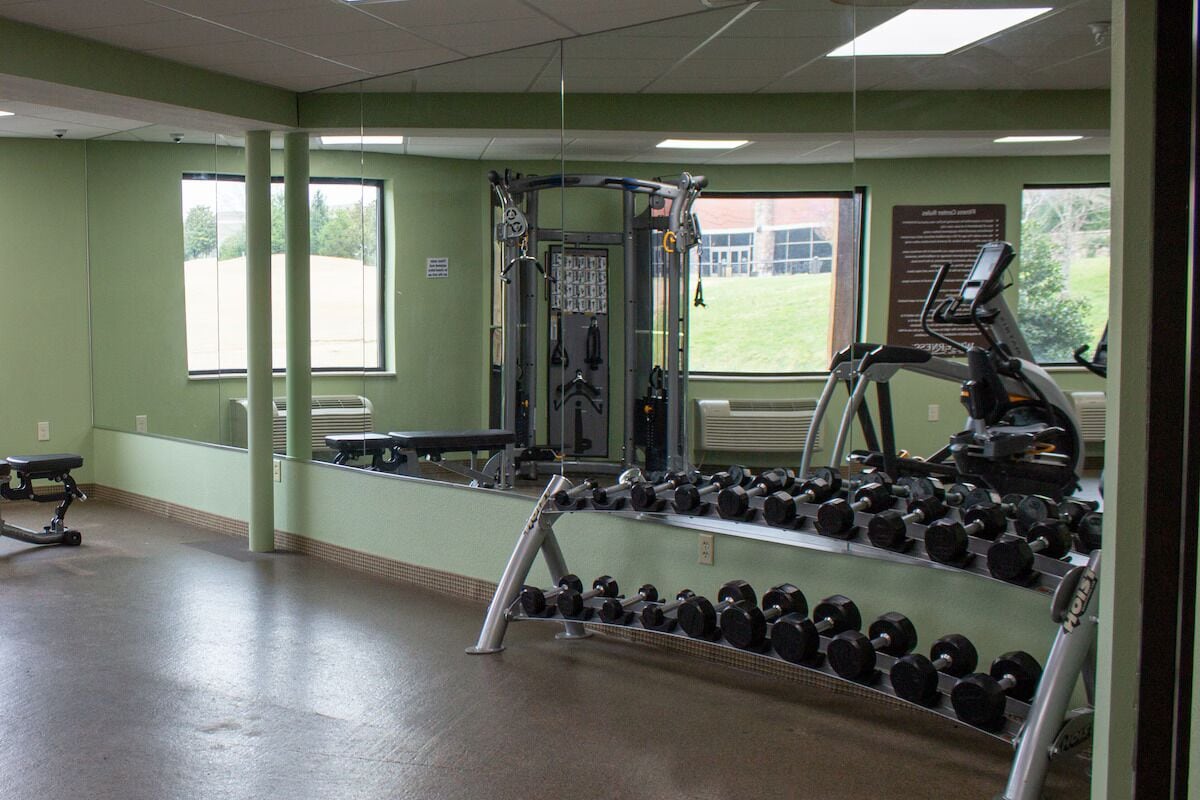 A gym with exercise equipment, a bench, and a rack of dumbbells.