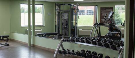 A gym with exercise equipment, a bench, and a rack of dumbbells.