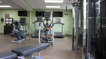 Een sportschool met loopbanden, elliptische trainers en een gewichtbank.
