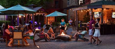 An outdoor seating area with tables and chairs, a fire pit, and string lights.