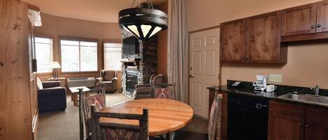 A cozy kitchen with wooden cabinets, a stone fireplace, and a dining area with a round table and chairs.