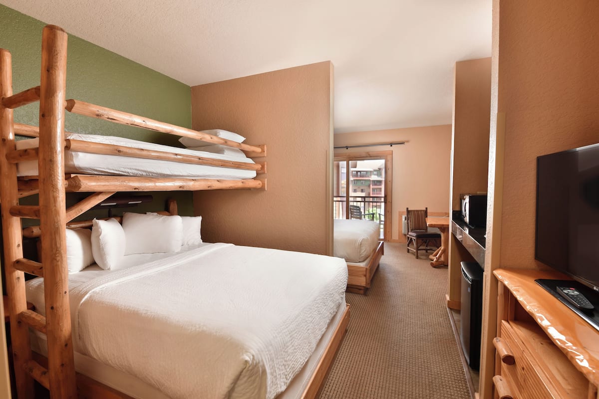 A hotel room with a bunk bed, a single bed, a television, and a desk.