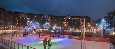 An outdoor ice skating rink with illuminated trees and a "SEASON'S GREETINGS" banner.
