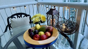Mesa de vidro com uma tigela de frutas e uma vela em uma varanda.