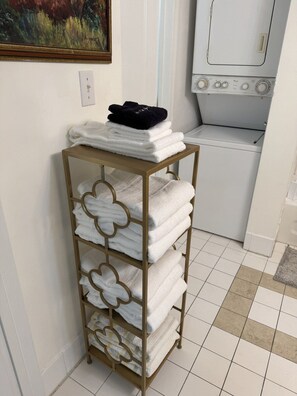 A bathroom with a white tiled floor, a gold towel rack with folded towels, a white washing machine, and a framed painting on the wall. - Suarez Art Stay, Brickell Bay View, Pool, Gym (Miami)