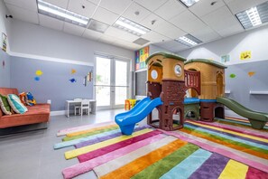 Espaço infantil com escorrega e estruturas de escalada, um sofá e um tapete listrado e colorido.