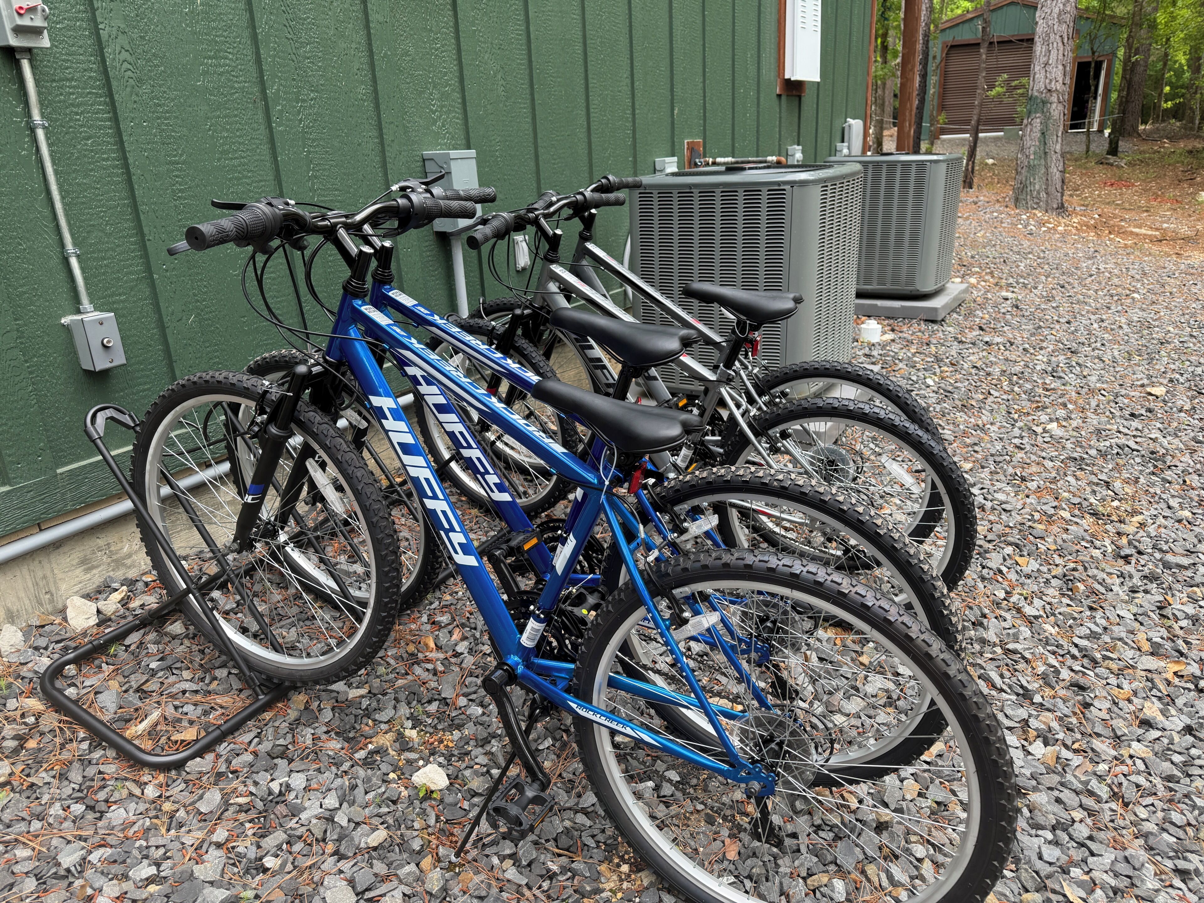 Bicycles parked on a gravel surface with a green wall and a building in the background.