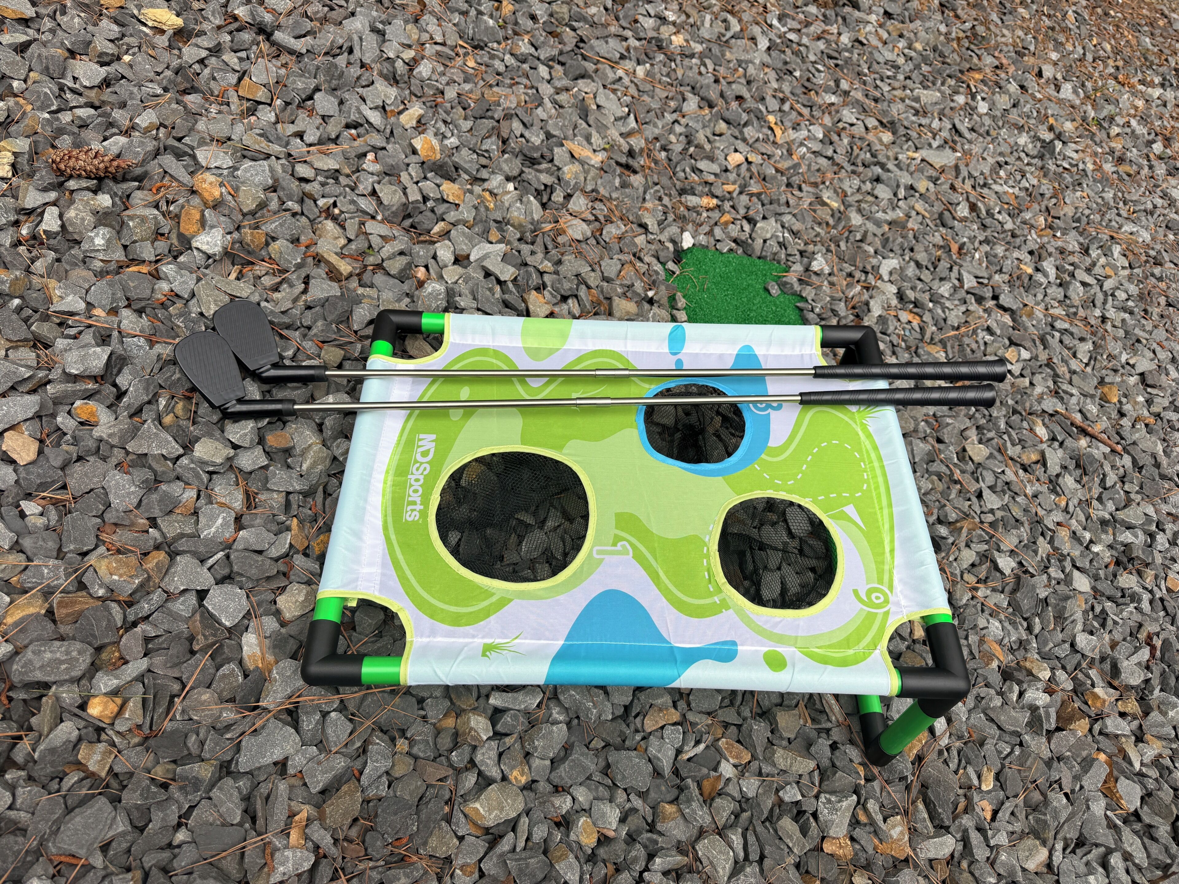 A portable camping stove with a green handle, a black pot, and a green fuel canister on a gravel surface.