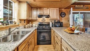 A kitchen with wooden cabinets, granite countertops, a stainless steel sink, a black stove, and a microwave.