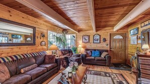 A cozy cabin interior with wooden walls, two leather sofas, a coffee table, and a door with a mirror.