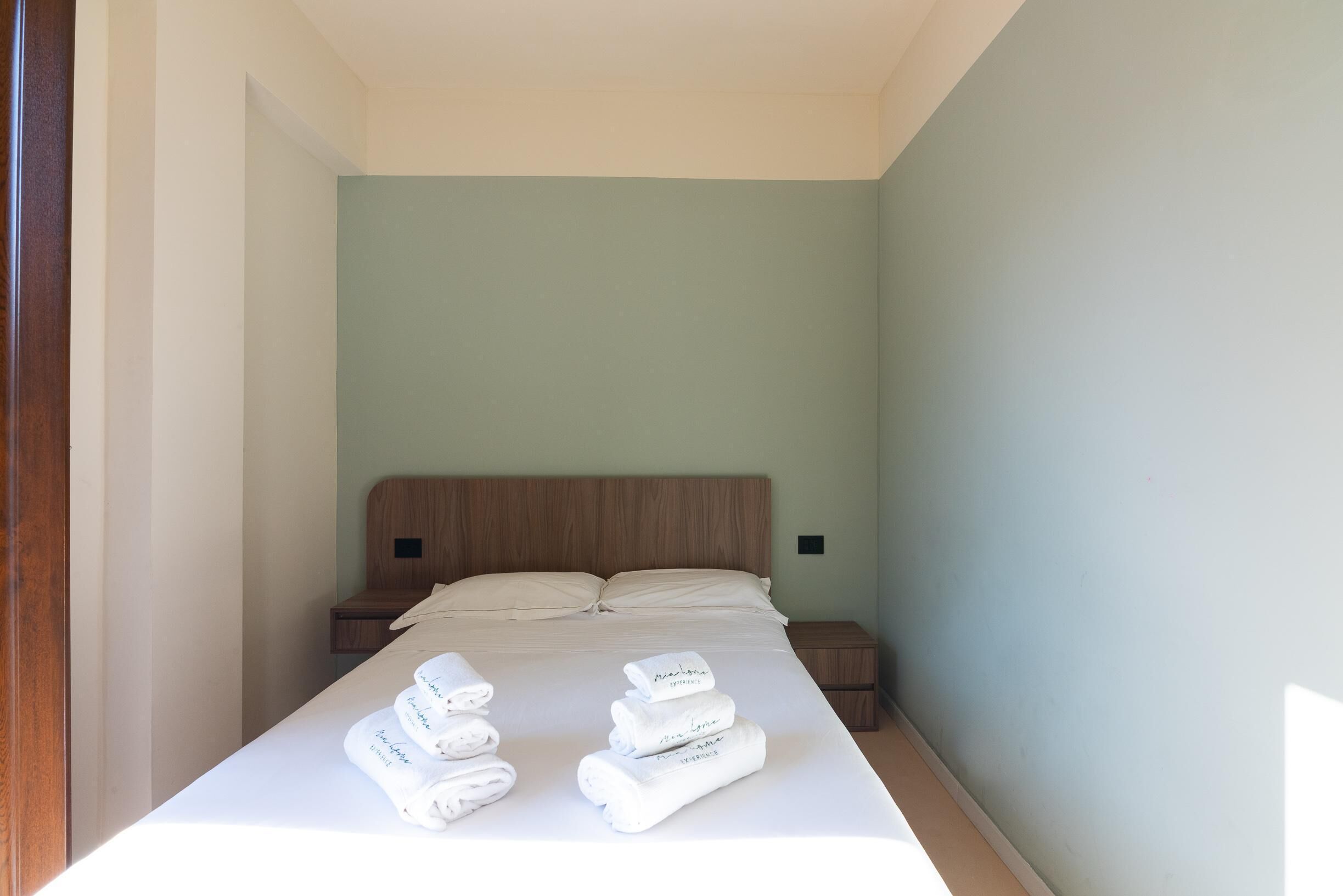 Een net opgemaakt bed met opgevouwen witte handdoeken en een houten hoofdbord.