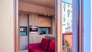 Une cuisine moderne avec des meubles en bois, un canapé rouge et un balcon agrémenté d’une chaise blanche.