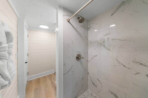 A modern bathroom with marble walls, a shower with a handheld showerhead, and a wooden floor. - Rustic Lodge • Pet-Friendly Cabin w/ Hot Tub & Fire Pit (Pigeon Forge)