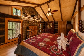A log cabin bedroom with a large bed, stone fireplace, and a ceiling fan. - Rustic Lodge • Pet-Friendly Cabin w/ Hot Tub & Fire Pit (Pigeon Forge)