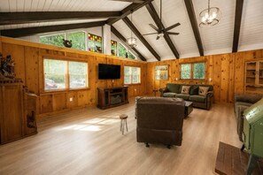 Un salon spacieux avec des murs en bois, un grand téléviseur et un ventilateur de plafond.