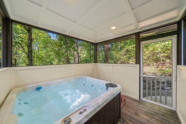 Ein Whirlpool in einem überdachten Außenbereich mit einer Holzterrasse und Blick auf Bäume.