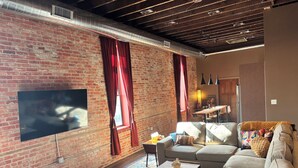 A living room with a brick wall, a flat-screen TV, a sofa, a coffee table, and a patterned rug.