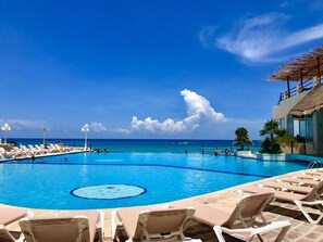 Una piscina con sillones, una estructura de techo de paja y vista al océano.