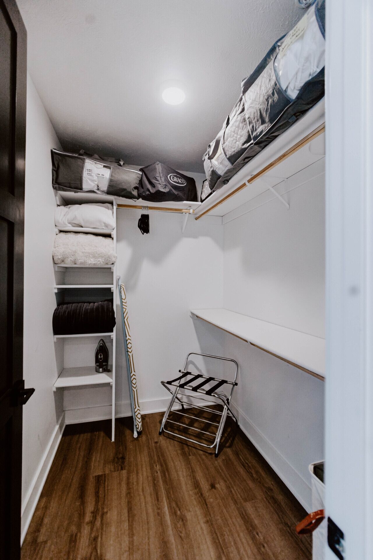 A compact storage room with shelves, a drying rack, and a small ironing board.