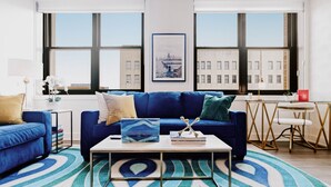 Una sala de estar moderna con un sofá azul, una mesa de centro con diseño geométrico y vistas a edificios a través de amplios ventanales.