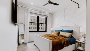 Un dormitorio moderno con cama, ventilador de techo, ventana y mesita de noche.