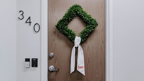 Una puerta de madera con un adorno de laurel verde y una cinta blanca, un teclado electrónico y un timbre.