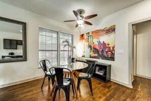 Comedor con una mesa redonda, cuatro sillas, un ventilador de techo y un cuadro abstracto grande en la pared.