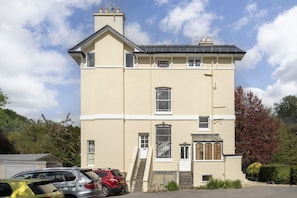 A two-story building with a beige facade, a central entrance with a glass door, and a staircase leading to the upper floor.