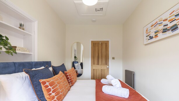 A neatly arranged bedroom with a bed, pillows, a mirror, a radiator, and a door.