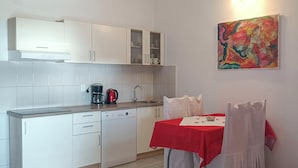 A compact kitchen with white cabinets, a coffee maker, and a dining area with a red tablecloth. - Lovely apartment in Maslenica with WiFi (Maslenica)