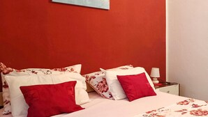 A room with a bed featuring floral bedding and red pillows, a nightstand with a lamp, and a painting on the wall. - Lovely apartment in Maslenica with WiFi (Maslenica)