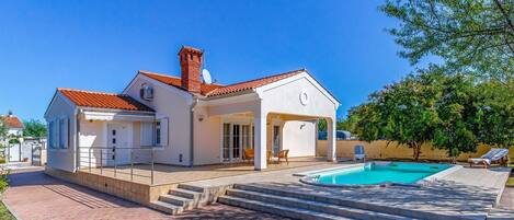 A two-story house with a swimming pool, a covered patio, and a garden.