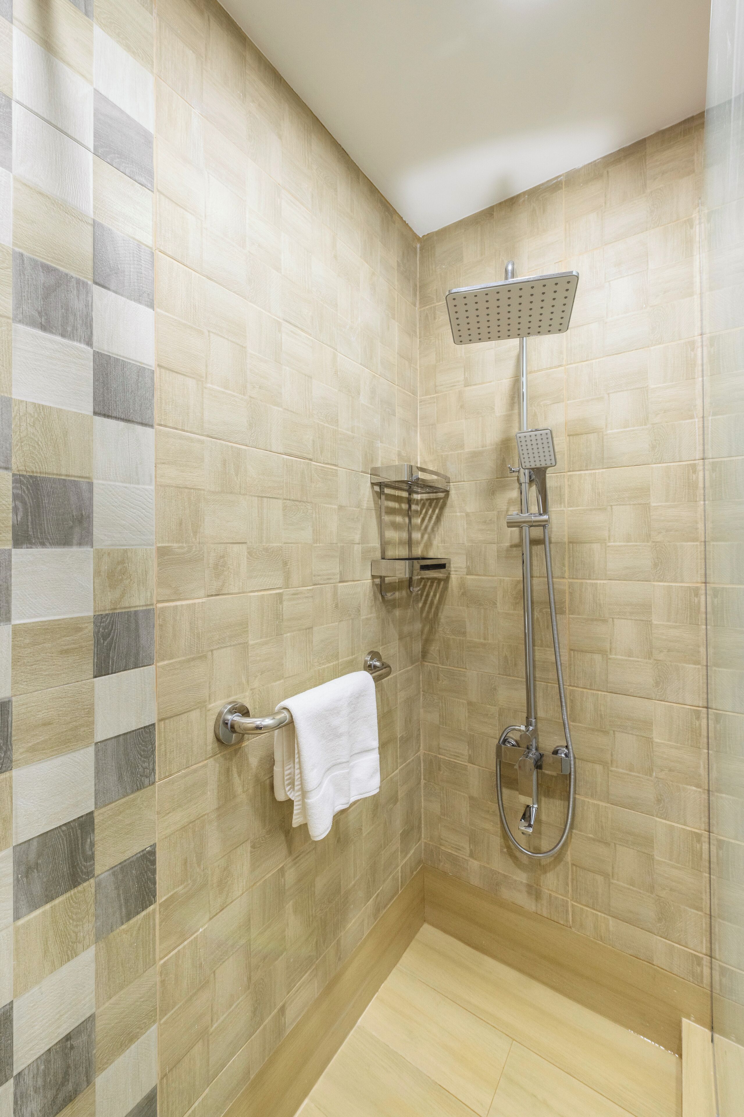A shower area with a handheld showerhead and a wall-mounted faucet, a towel rack with a white towel, and a corner shelf unit.