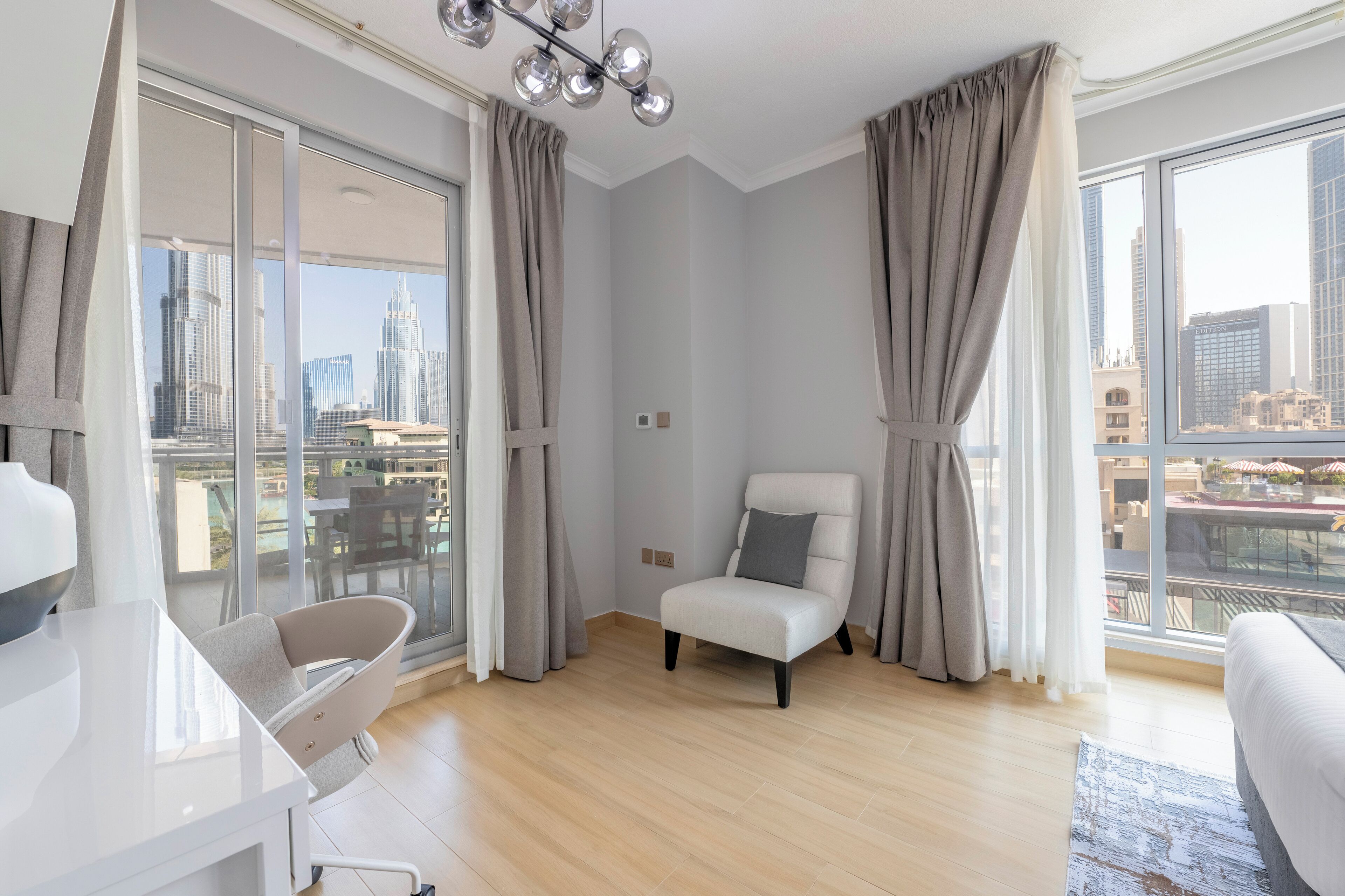 Una camera d'albergo moderna con una grande finestra che si affaccia sulla città, una poltrona bianca e un tavolino.