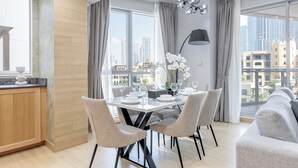 Ett modernt matområde med ett bord för fyra personer, stora fönster med gardiner och utsikt över stadens byggnader.